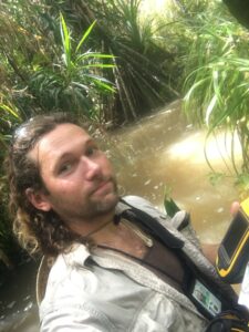 biologist Joshua Brown standing in deep forest river holding a GPS navigator surveying for little fire ants on Guam at the Naval Base